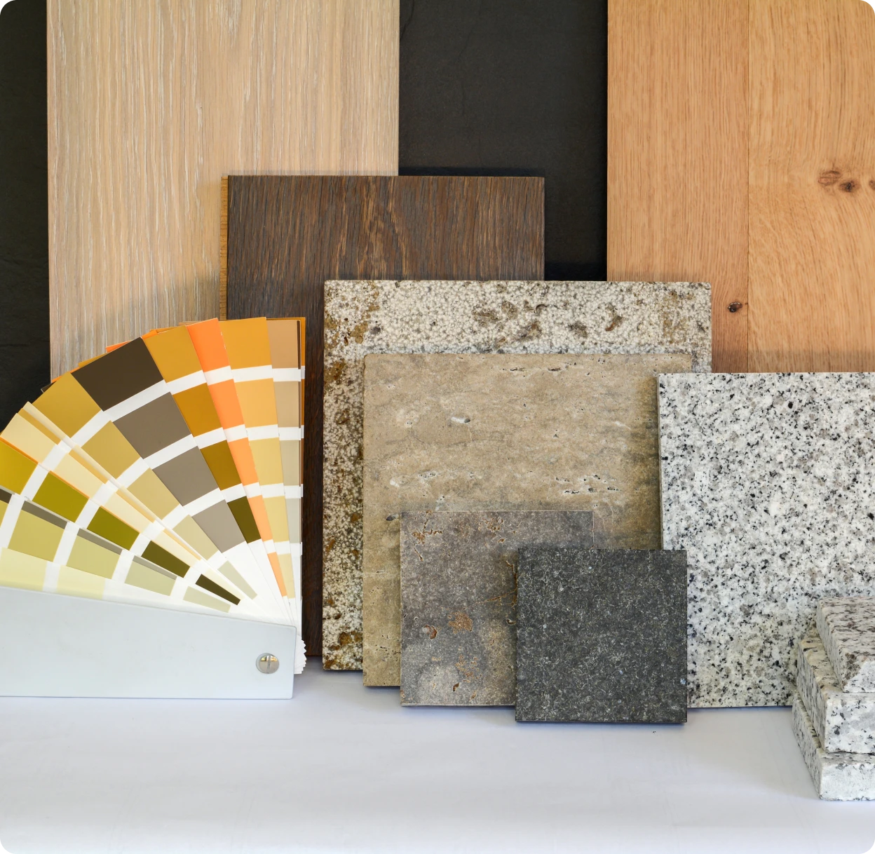 Various flooring samples displayed, including wood, stone, and granite textures, with a fan of color swatches in shades of yellow, brown, and orange in the foreground.